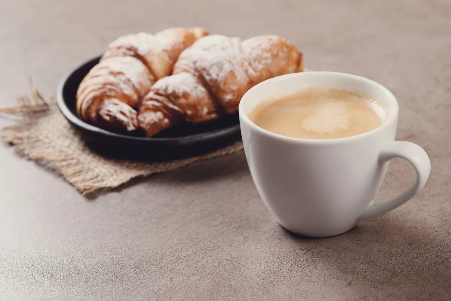 Two croissants and a cup of coffe placed on a brown table